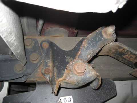 1996 Ford Bronco - Close-up view of a corroded metal bracket assembly attached to a vehicle's undercarriage.