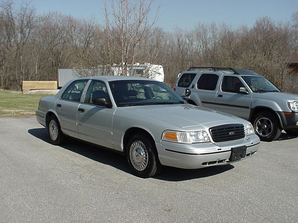 Silver 2000 Ford Crown Victoria sedan, 3q front view, parked next to an SUV