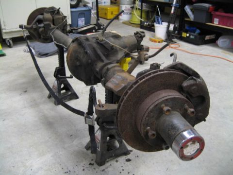 1996 Ford Bronco - Front axle assembly, likely from a truck or SUV, is supported by jack stands in a garage setting.