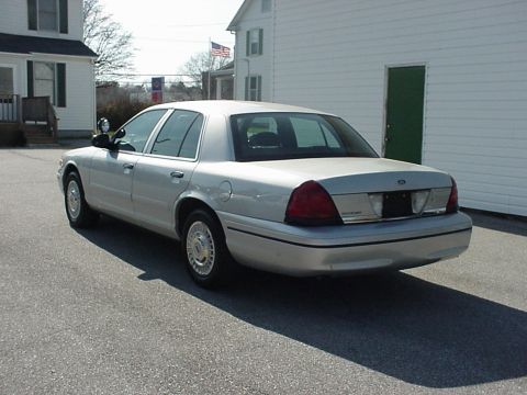 2000 Ford Crown Victoria - A silver sedan is parked on an asphalt surface near a white building with a green door.