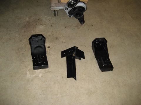 1996 Ford Bronco - Three black suspension brackets are laid out on a concrete floor, possibly for a vehicle modification.