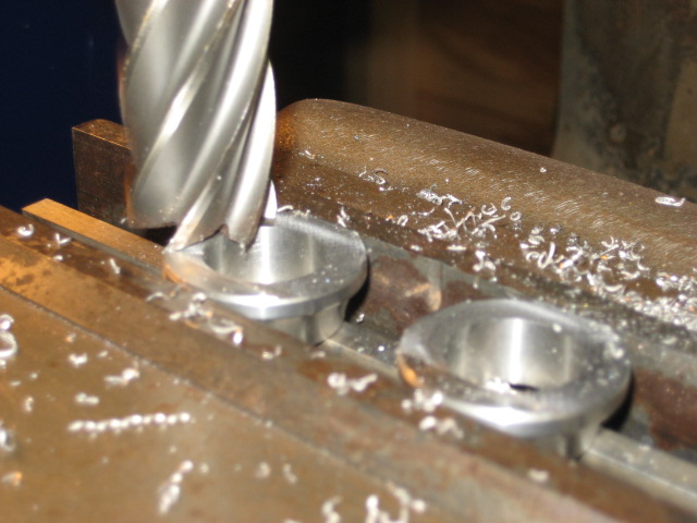 Close-up of a milling machine cutting two metal cylindrical parts with shavings scattered