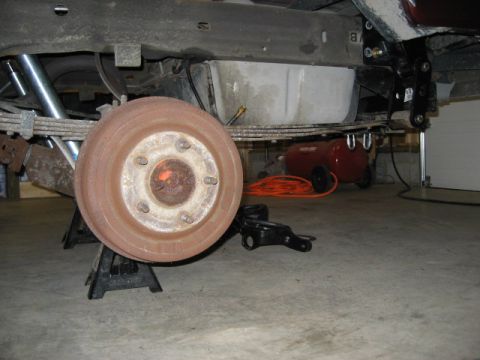 1996 Ford Bronco - Close-up of a vehicle's rear drum brake assembly and suspension components, supported by jack stands in a garage.