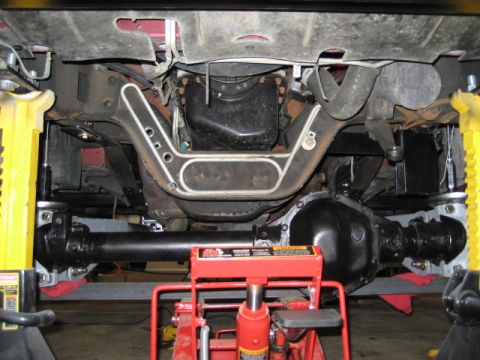 1996 Ford Bronco - The underside of a vehicle is shown, supported by jack stands and a hydraulic jack, with focus on the drivetrain and suspension.