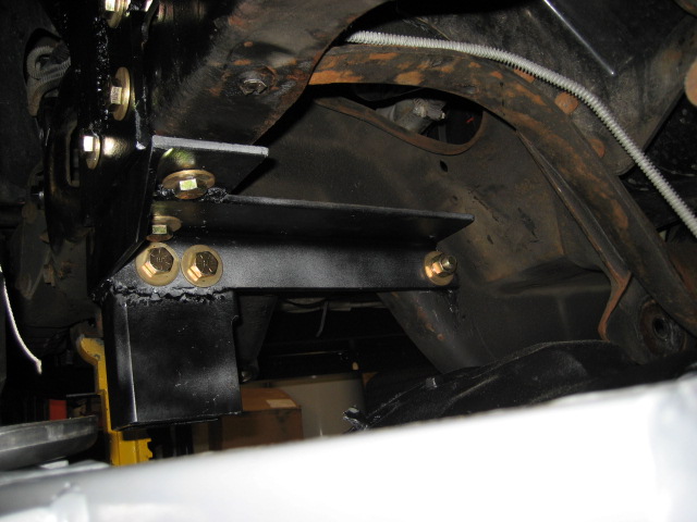 Black metal bracket bolted to rusty vehicle frame with gold colored bolts