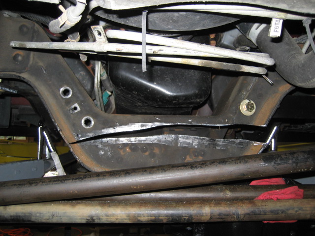 Close-up of vehicle undercarriage showing suspension and frame components. Red rags are visible