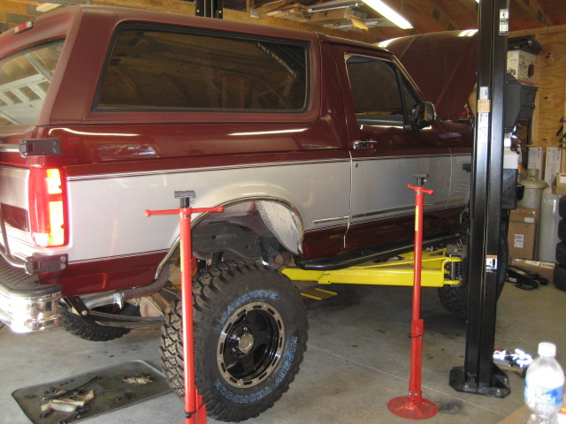 Maroon and silver 1996 Ford Bronco on a yellow car lift in a garage