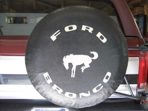 1996 Ford Bronco - A spare tire cover with the Ford Bronco logo is mounted on the rear of a maroon SUV.