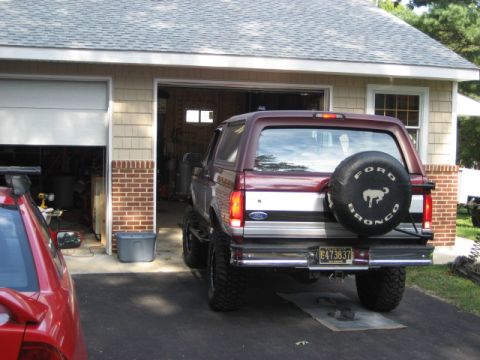 1996 Ford Bronco - Rear view of a maroon 1996 Ford Bronco with a spare tire on the back, parked in front of a garage.