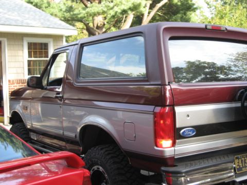 1996 Ford Bronco - This two-tone Ford Bronco is parked in a driveway with a house and trees in the background.