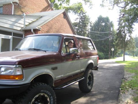 1996 Ford Bronco - A man in a maroon and silver Ford Bronco gives a peace sign from the driver's seat.