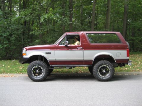 1996 Ford Bronco - Side view of a lifted Ford Bronco with two-tone paint and aftermarket wheels.