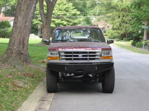 1996 Ford Bronco - This maroon Ford F-150 pickup truck is parked on a street with trees and houses in the background.
