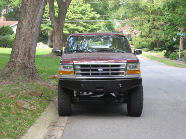 Front view of a maroon Ford F-150 pickup truck with a custom bumper and large tires parked on a residential street