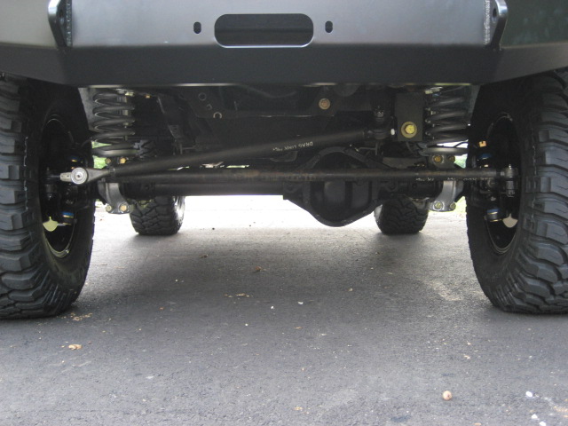 Undercarriage view showing front axle, steering linkage, and suspension components of a modified SUV with large tires
