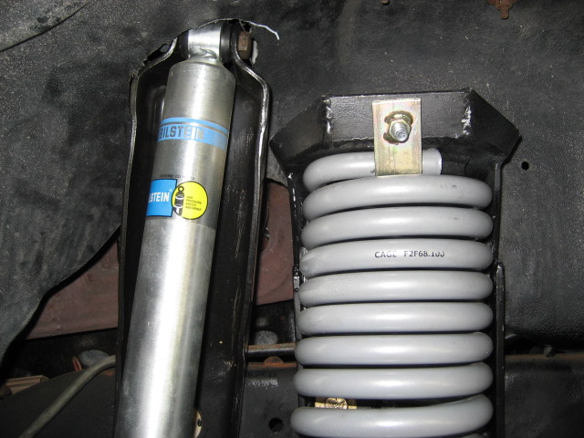 Bilstein shock absorber next to a gray coil spring with CAGE F2F68.103 stamped on it