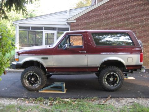 1996 Ford Bronco - Side view of a lifted 1996 Ford Bronco with two-tone paint and off-road tires.