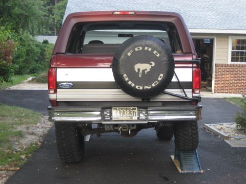 1996 Ford Bronco - The rear of a Ford Bronco is shown parked in a driveway, with a spare tire mounted on the tailgate.