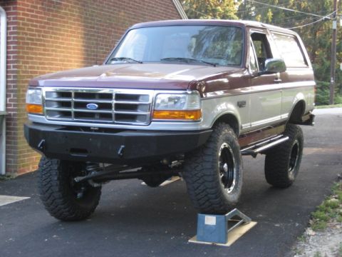 1996 Ford Bronco - A modified Ford Bronco sits on a driveway with its front passenger tire elevated on a blue ramp.