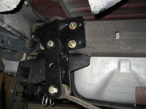 1996 Ford Bronco - Close-up view of a black suspension bracket and fuel tank on a vehicle's undercarriage.