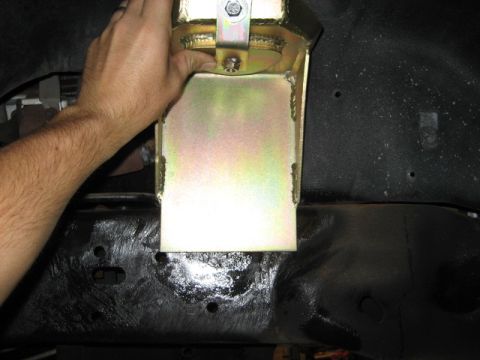 1996 Ford Bronco - A hand installs a yellow metal suspension bracket onto the frame of a vehicle, likely for off-road modification.