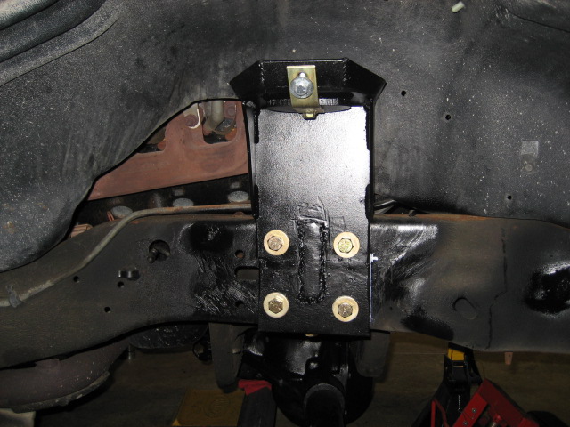 Close-up of a black metal bracket with four bolts attached to a vehicle's frame
