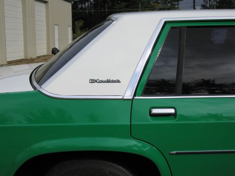 1991 Ford LTD Crown Victoria - Close-up of the rear quarter window and C-pillar of a green and white sedan showing a Crown Victoria nameplate badge.