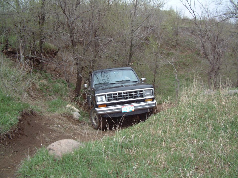 Dark gray 1980s Ford Bronco II descending a rutted dirt trail on a brushy hillside