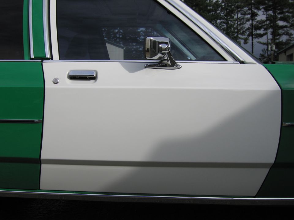 Close-up of white front door and chrome mirror on a green and white sedan