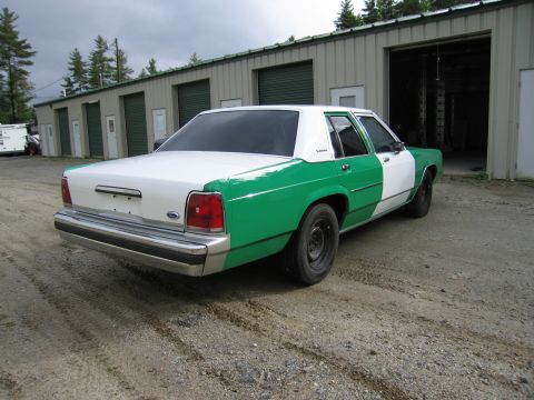 1991 Ford LTD Crown Victoria - Rear three-quarter view of a green and white full-size Ford sedan with chrome bumper and Ford trunk badge on a gravel lot.