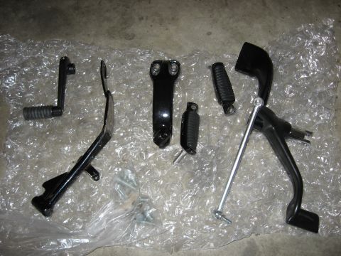 2004 Harley-Davidson Sportster Custom - Various motorcycle foot controls and hardware are displayed on bubble wrap, with a 'SuperMotors' logo visible.