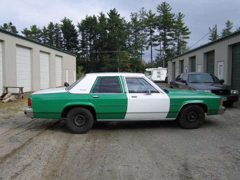 1991 Ford LTD Crown Victoria - Driver-side profile of a green and white full-size Ford sedan parked on gravel beside storage units and a dark SUV.