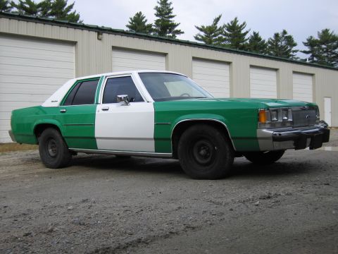 1991 Ford LTD Crown Victoria - Front three-quarter view of a green and white full-size Ford sedan with a chrome grille and Ford emblem on a gravel lot.