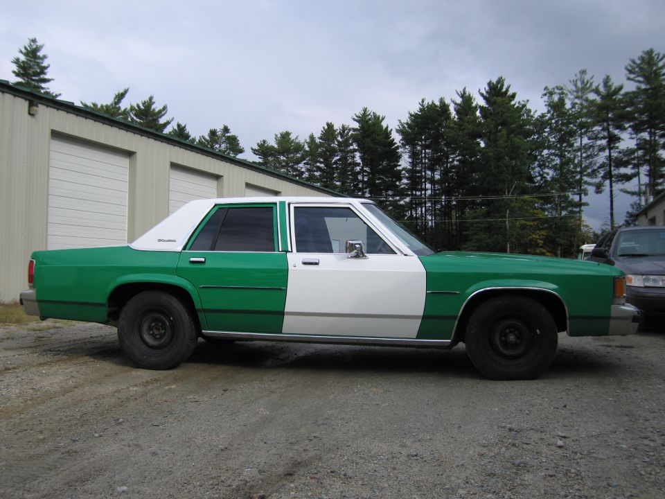 Passenger-side profile of a green and white Ford sedan on a gravel lot