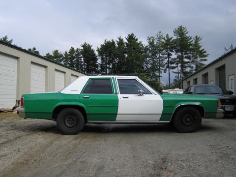 1991 Ford LTD Crown Victoria - Driver-side profile of a green-and-white two-tone full-size Ford sedan parked on a gravel lot in front of metal storage buildings.