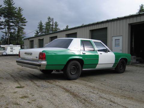 1991 Ford LTD Crown Victoria - Rear three-quarter passenger-side view of a green-and-white full-size Ford sedan, Ford oval on the trunk, parked by metal garage doors.
