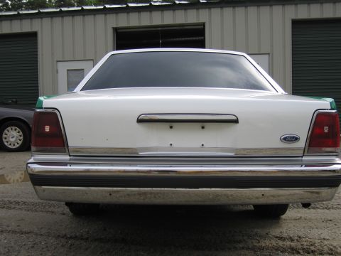 1991 Ford LTD Crown Victoria - Straight-on rear view of a white full-size Ford sedan with green edges, Ford oval and full chrome bumper, on a gravel lot.