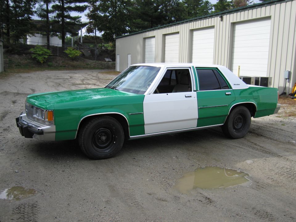 Front three-quarter driver view of green and white full-size Ford sedan on gravel