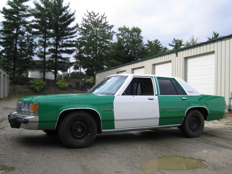 1991 Ford LTD Crown Victoria - Front three-quarter driver-side view of a green-and-white two-tone full-size Ford sedan parked on gravel beside a metal building and trees.
