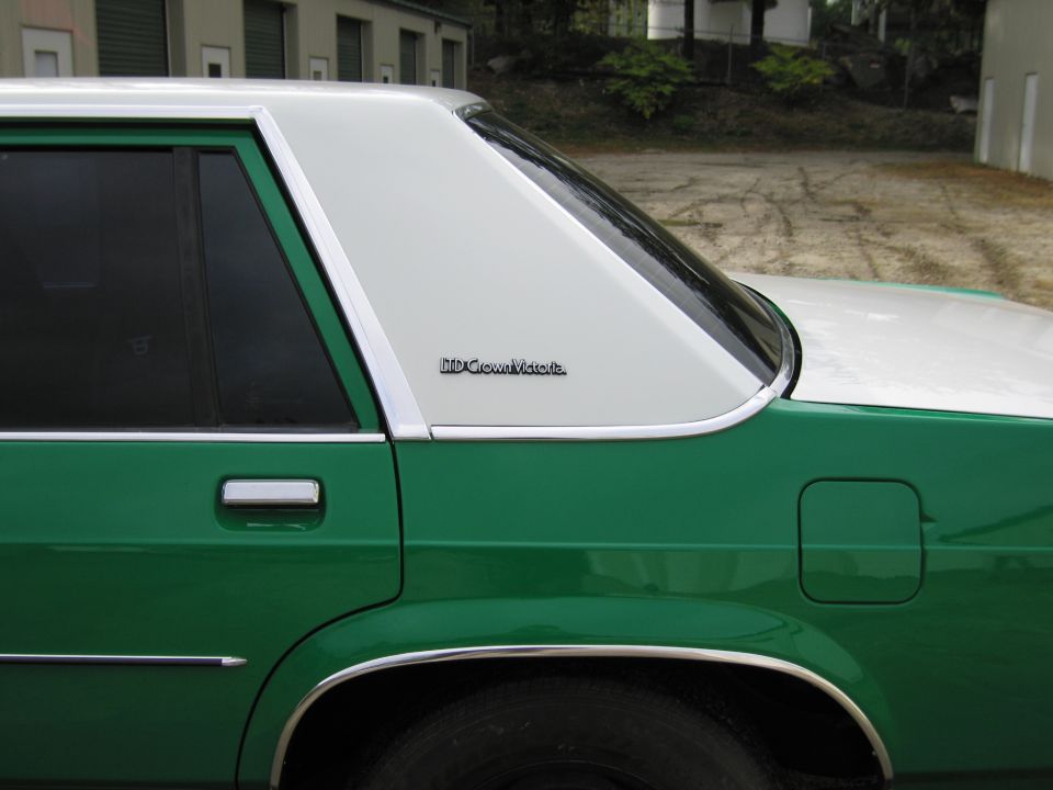 Rear quarter window of green and white Ford with LTD Crown Victoria badge