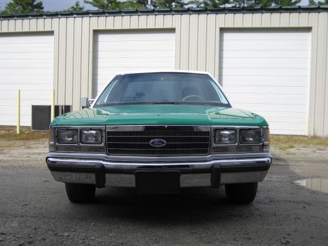 1991 Ford LTD Crown Victoria - Straight-on front view of a green full-size Ford sedan with white roof, Ford grille emblem and stacked dual rectangular headlights.