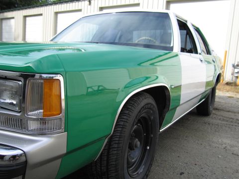 1991 Ford LTD Crown Victoria - Front quarter close-up of a green-and-white full-size Ford sedan showing the amber turn signal, fender and black steel wheel.