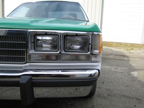 1991 Ford LTD Crown Victoria - Close-up of the green front end of a Ford sedan showing the dual rectangular headlights, amber marker and chrome bumper.