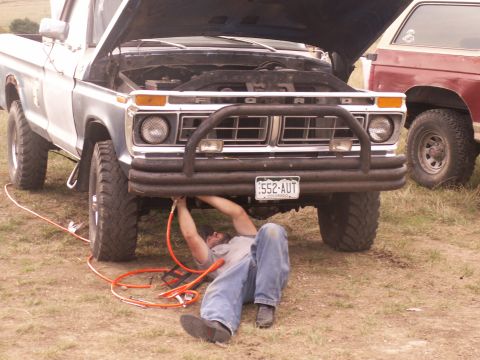 1977 Ford F-250 - Man works on the engine of a 1977 Ford F-250, with another truck visible in the background.
