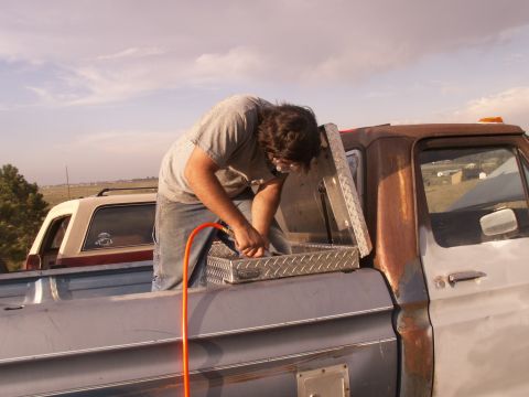 1977 Ford F-250 - A man works on a toolbox in the bed of a 1977 Ford F-250, with another vehicle visible in the background.