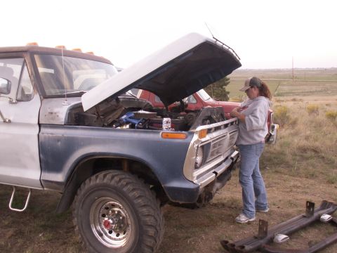 1977 Ford F-250 - A person works on the engine of a large truck with the hood open. Another vehicle is visible in the background.