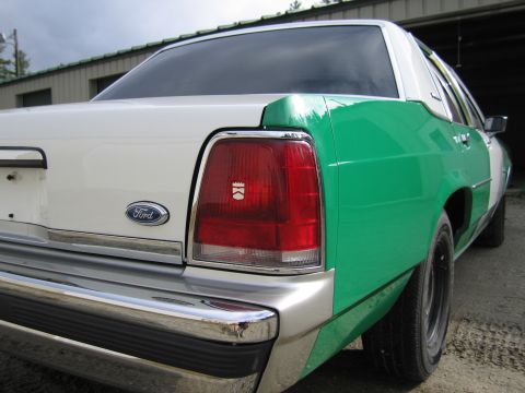 1991 Ford LTD Crown Victoria - Rear quarter close-up of a green-and-white full-size Ford sedan showing the Ford oval, red taillight and chrome bumper.