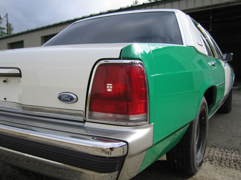 Rear quarter close-up of green and white Ford sedan with Ford emblem taillight