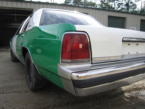 1991 Ford LTD Crown Victoria - Rear quarter view of a green-and-white full-size Ford sedan showing the red taillight, decklid and chrome bumper on a gravel lot.