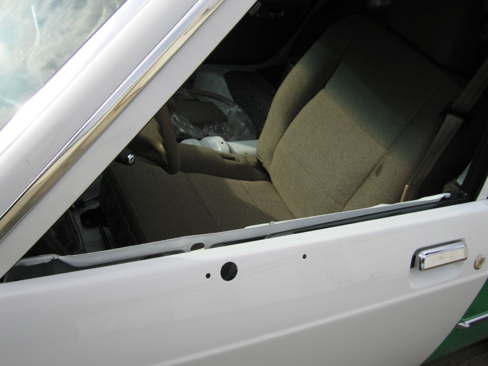 Open door of white Ford sedan showing tan cloth front seats interior